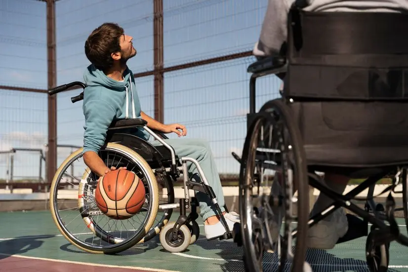 A young man in a wheelchair holds a basketball on his lap, looking upwards