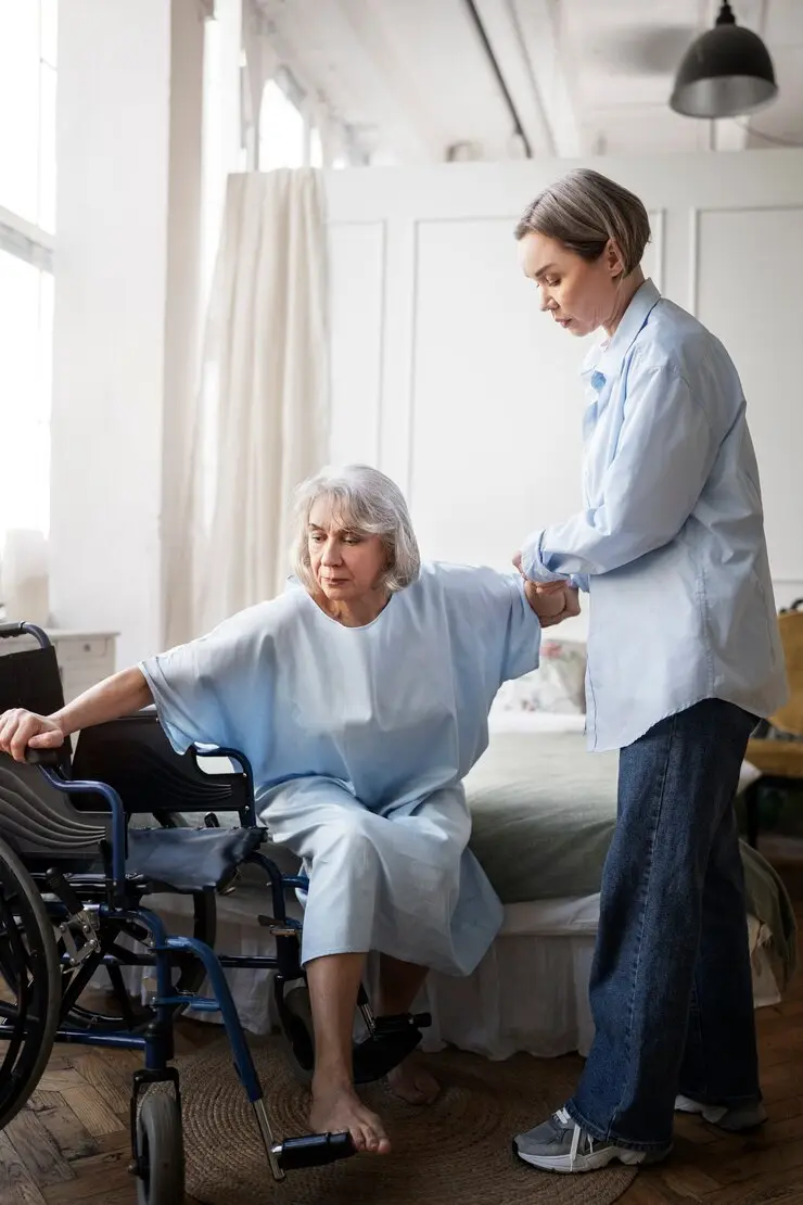 Healthcare professional assisting elderly woman transitioning from bed to wheelchair in a well-lit room