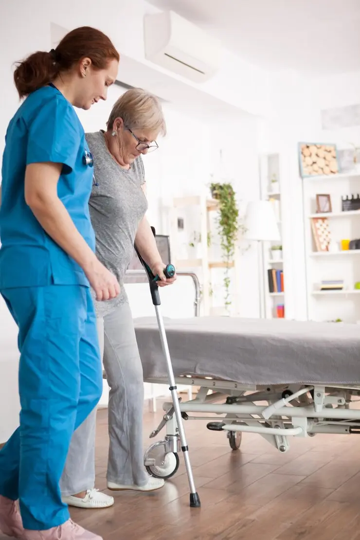 Healthcare worker in blue attire assisting an elderly woman using a walking aid in a modern room setting